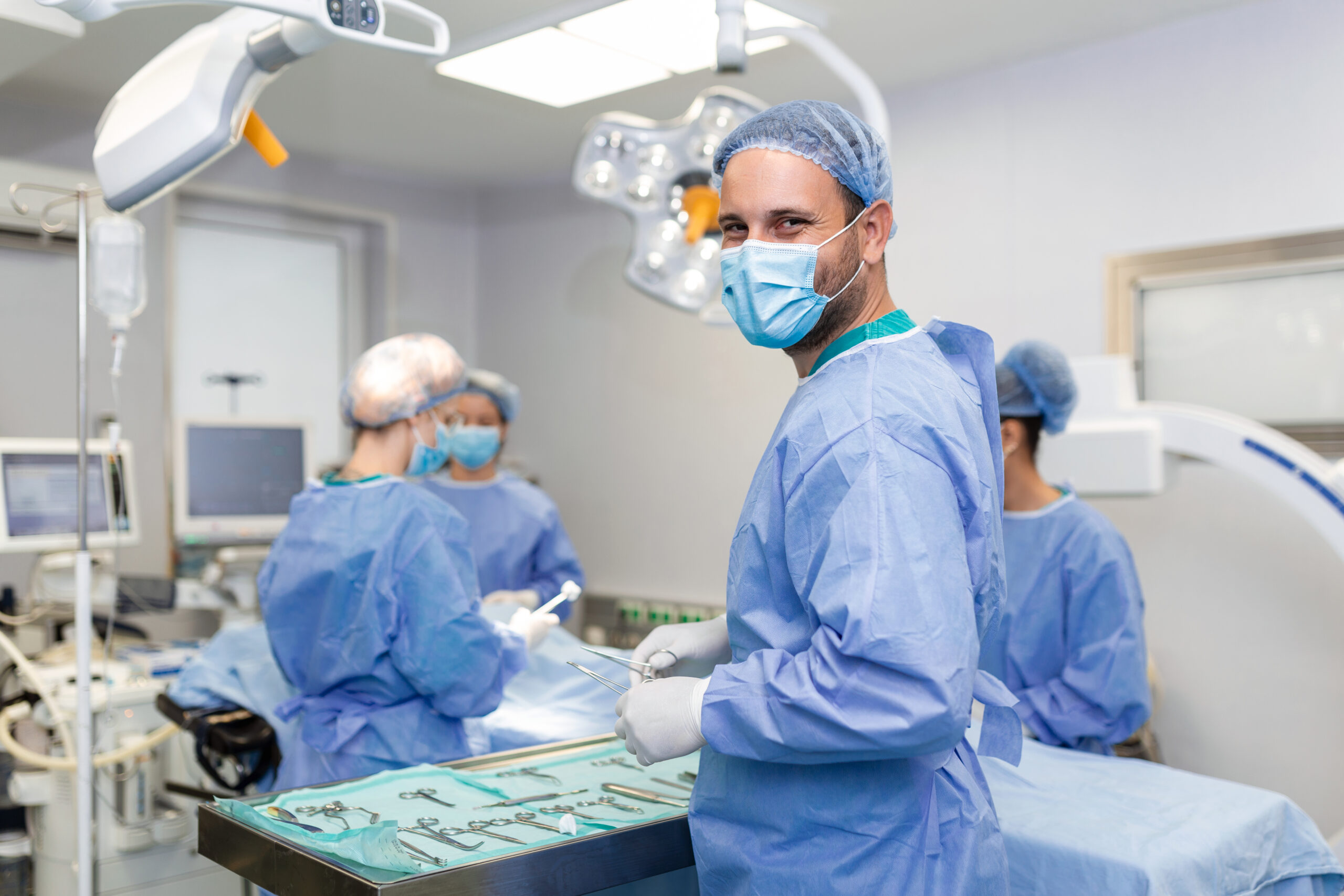 Portrait of happy man surgeon standing in operating room, ready to work on a patient. Male medical worker in surgical uniform in operation theater.